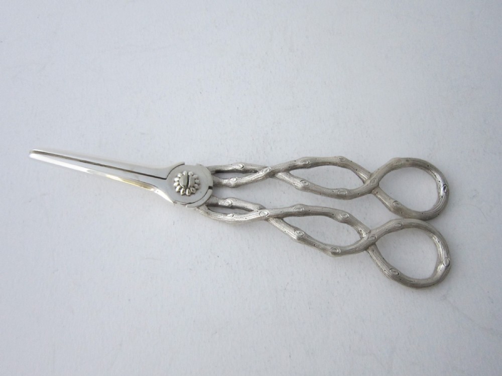 A pair of Victorian sterling silver grape scissors with grapevine-textured handles, resting inside an open fitted presentation case. View III