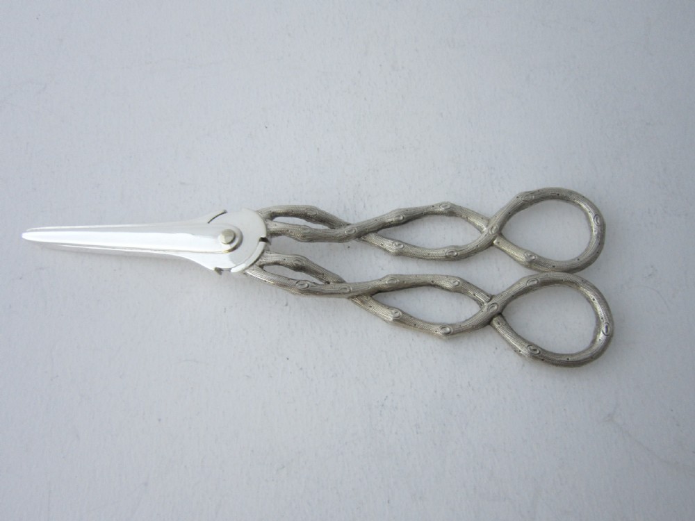 A pair of Victorian sterling silver grape scissors with grapevine-textured handles, resting inside an open fitted presentation case. View IV