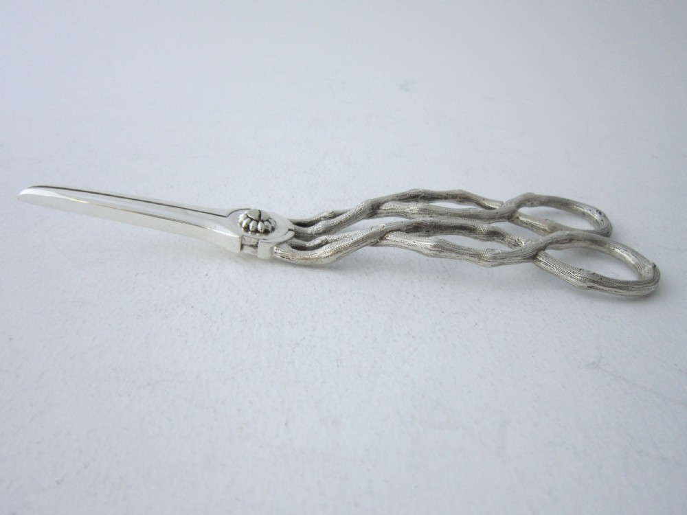 A pair of Victorian sterling silver grape scissors with grapevine-textured handles, resting inside an open fitted presentation case. View V