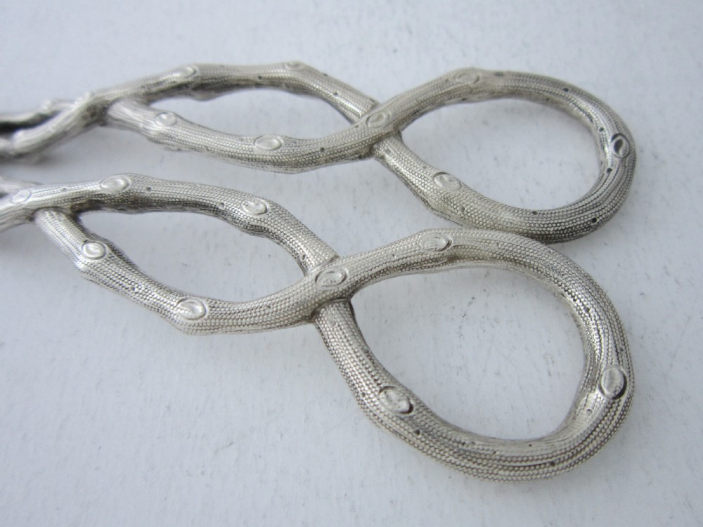 A pair of Victorian sterling silver grape scissors with grapevine-textured handles, resting inside an open fitted presentation case. View VII