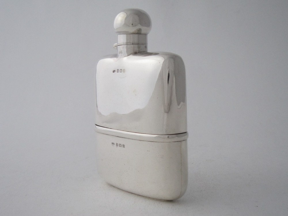 A curved George V sterling silver hip flask featuring a detachable lower cup and a round bayonet cap against a plain studio background.