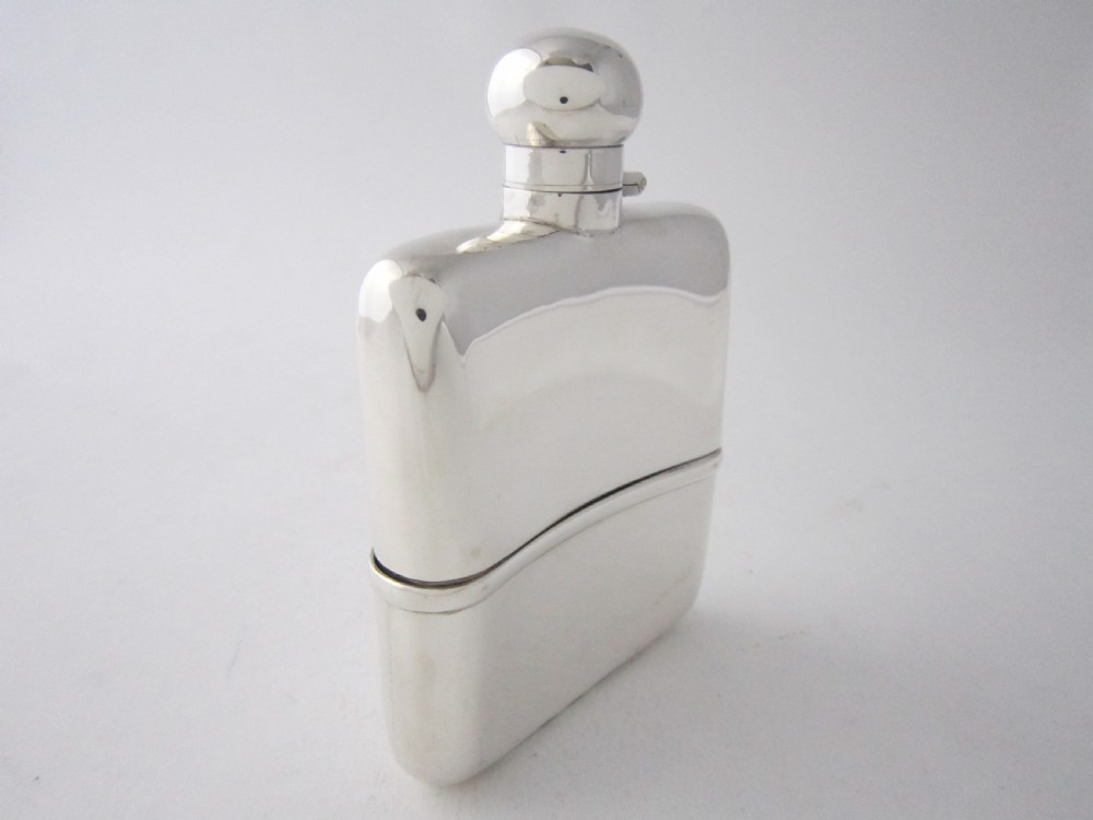 A curved George V sterling silver hip flask featuring a detachable lower cup and a round bayonet cap against a plain studio background. View II
