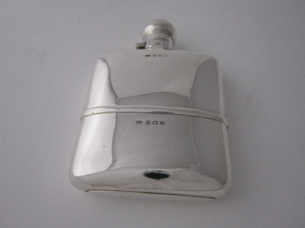 A curved George V sterling silver hip flask featuring a detachable lower cup and a round bayonet cap against a plain studio background. View V