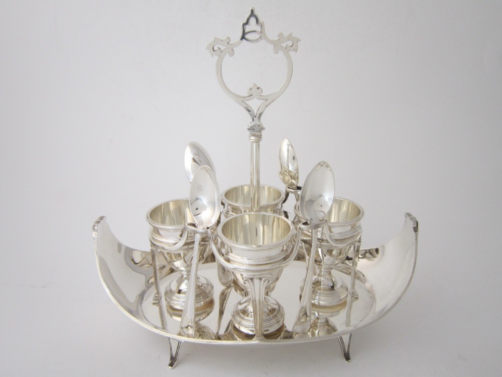 A George V sterling silver egg cruet set featuring four egg cups and matching spoons arranged on an oval silver tray with a central loop handle.