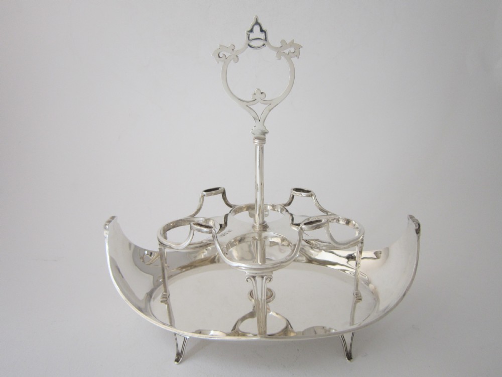 A George V sterling silver egg cruet set featuring four egg cups and matching spoons arranged on an oval silver tray with a central loop handle. View IV