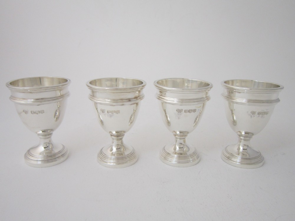 A George V sterling silver egg cruet set featuring four egg cups and matching spoons arranged on an oval silver tray with a central loop handle. View VI