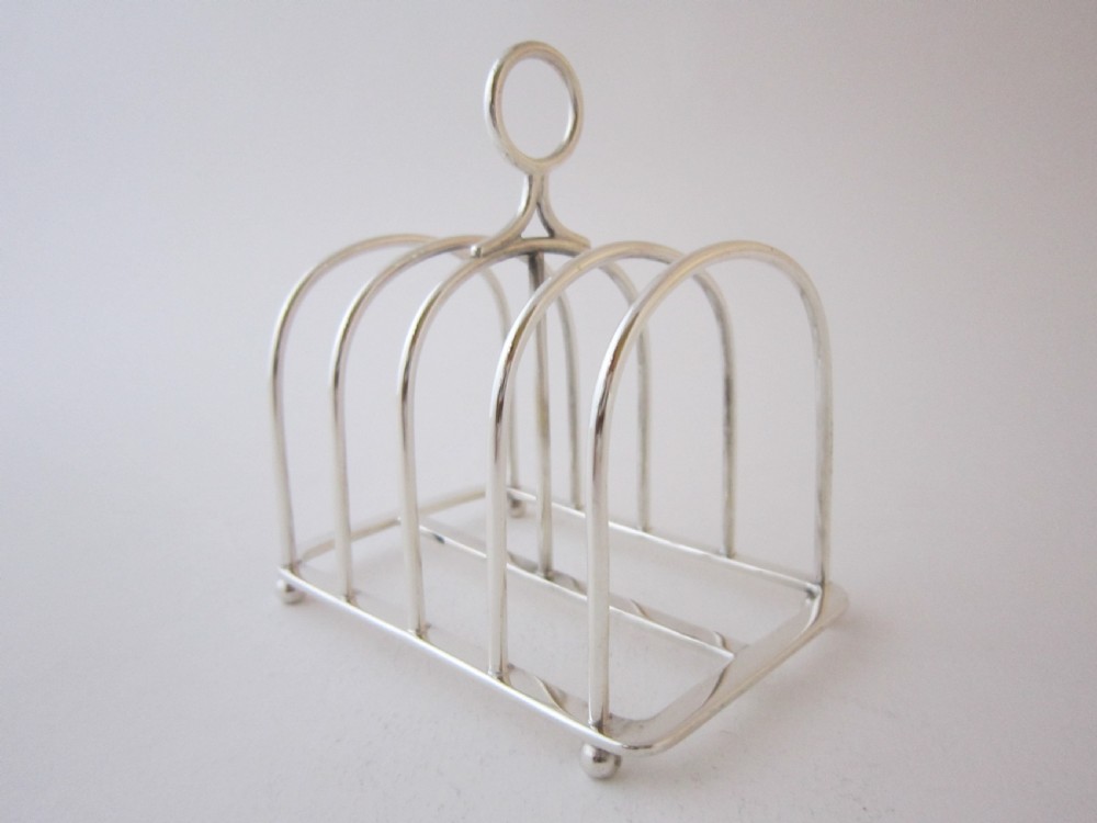 A Victorian sterling silver toast rack featuring arched wire dividers, a top loop handle, and four small ball feet.