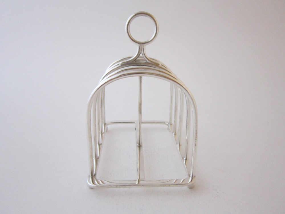 A Victorian sterling silver toast rack featuring arched wire dividers, a top loop handle, and four small ball feet. View II
