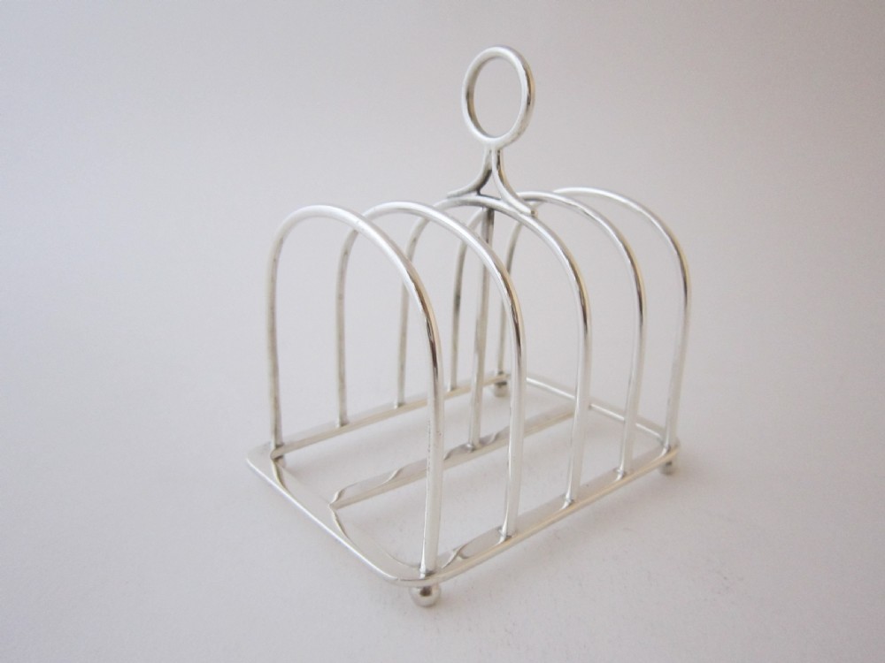 A Victorian sterling silver toast rack featuring arched wire dividers, a top loop handle, and four small ball feet. View III