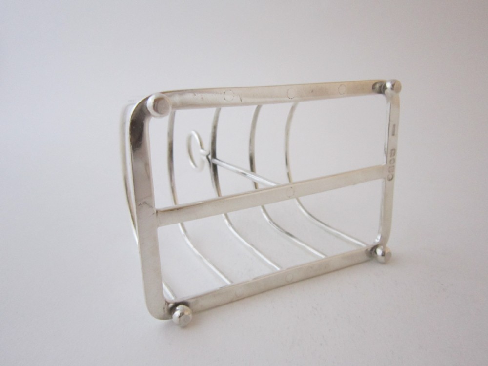 A Victorian sterling silver toast rack featuring arched wire dividers, a top loop handle, and four small ball feet. View V