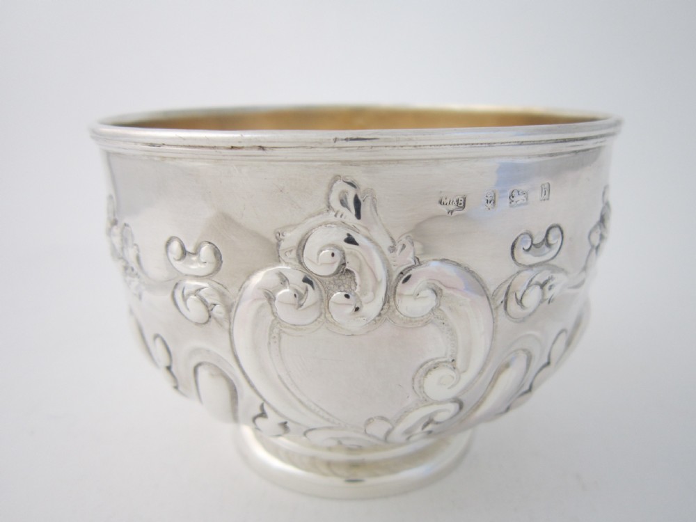 An Edwardian sterling silver bowl featuring repousse scroll motifs, a gilded interior, a raised foot rim, and visible English hallmarks.