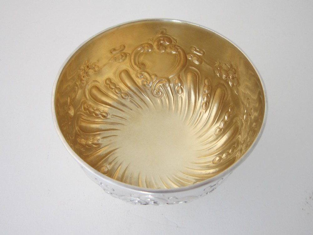 An Edwardian sterling silver bowl featuring repousse scroll motifs, a gilded interior, a raised foot rim, and visible English hallmarks. View V