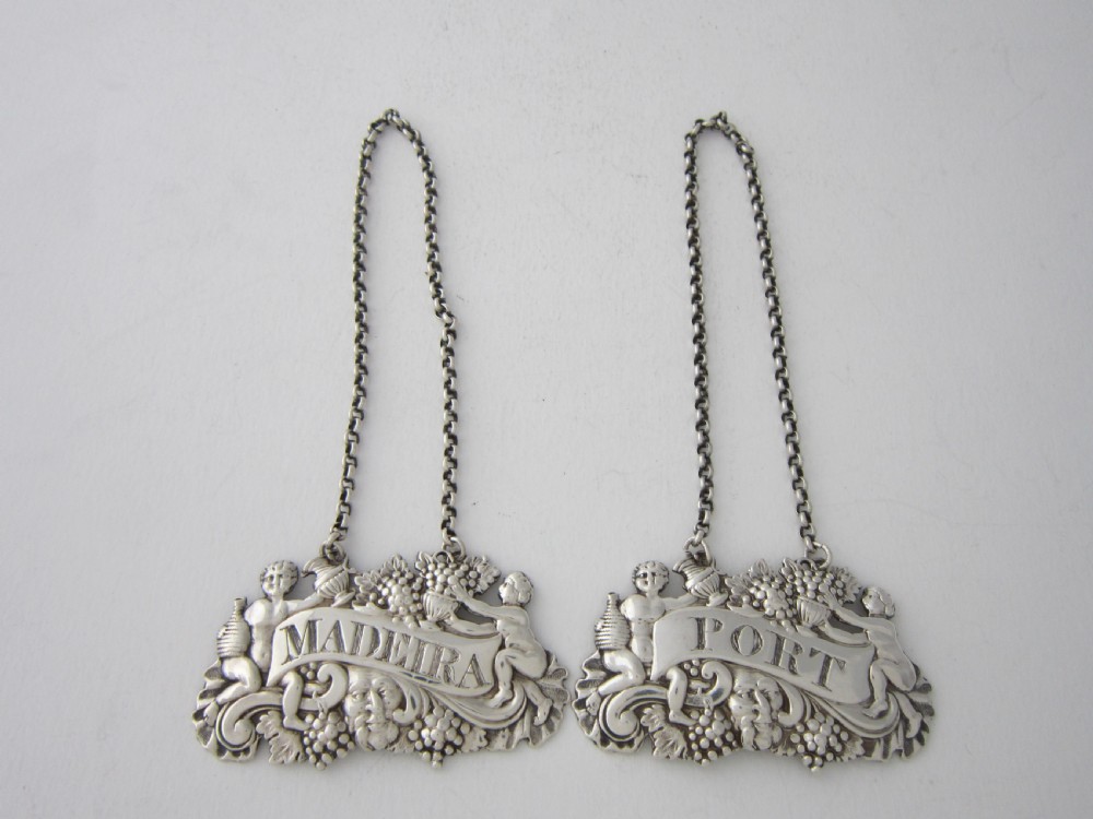 A pair of Scottish George III sterling silver decanter labels engraved with Madeira and Port, featuring relief motifs of cherubs, grapes, and scrollwork on hanging chains. View II