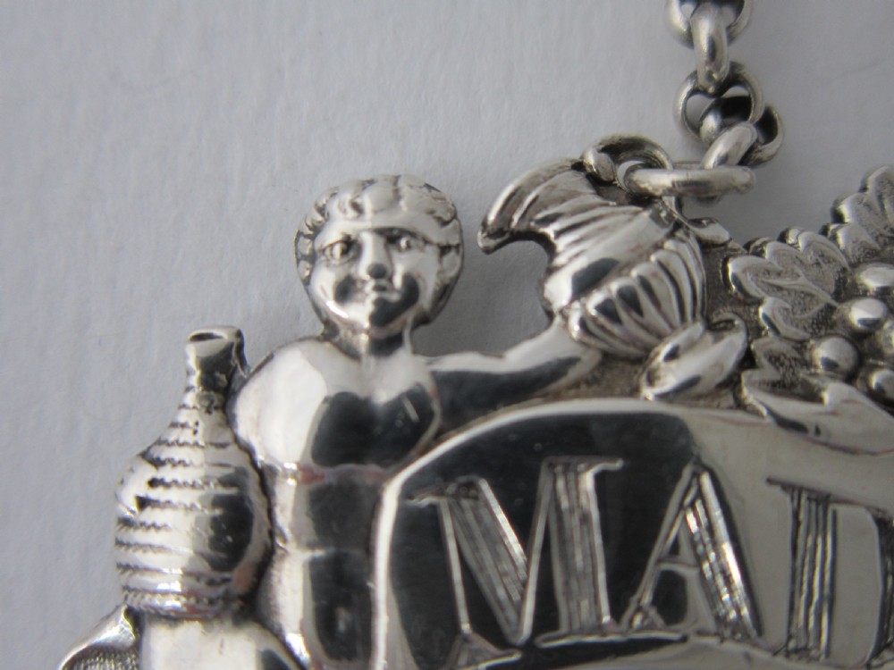 A pair of Scottish George III sterling silver decanter labels engraved with Madeira and Port, featuring relief motifs of cherubs, grapes, and scrollwork on hanging chains. View IV