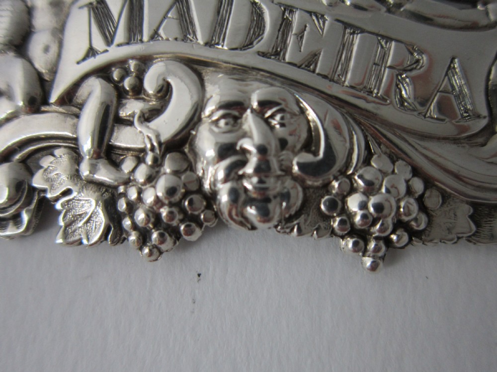 A pair of Scottish George III sterling silver decanter labels engraved with Madeira and Port, featuring relief motifs of cherubs, grapes, and scrollwork on hanging chains. View V