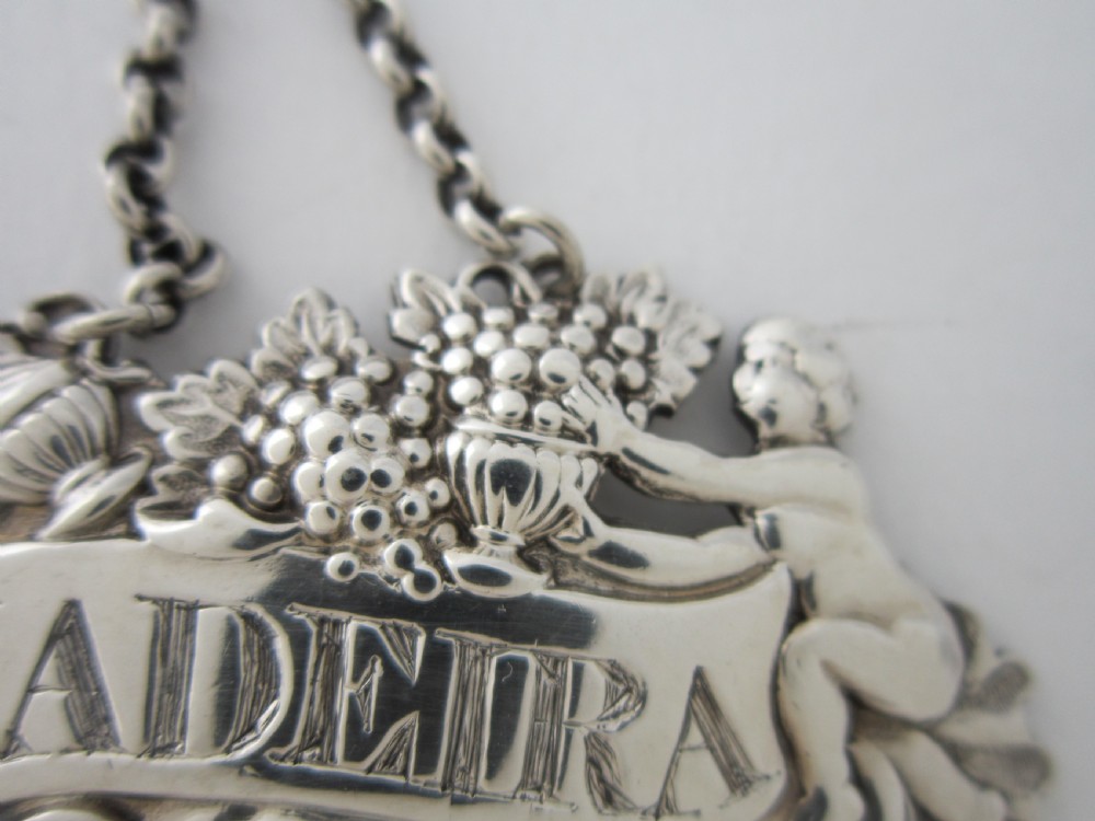 A pair of Scottish George III sterling silver decanter labels engraved with Madeira and Port, featuring relief motifs of cherubs, grapes, and scrollwork on hanging chains. View VI