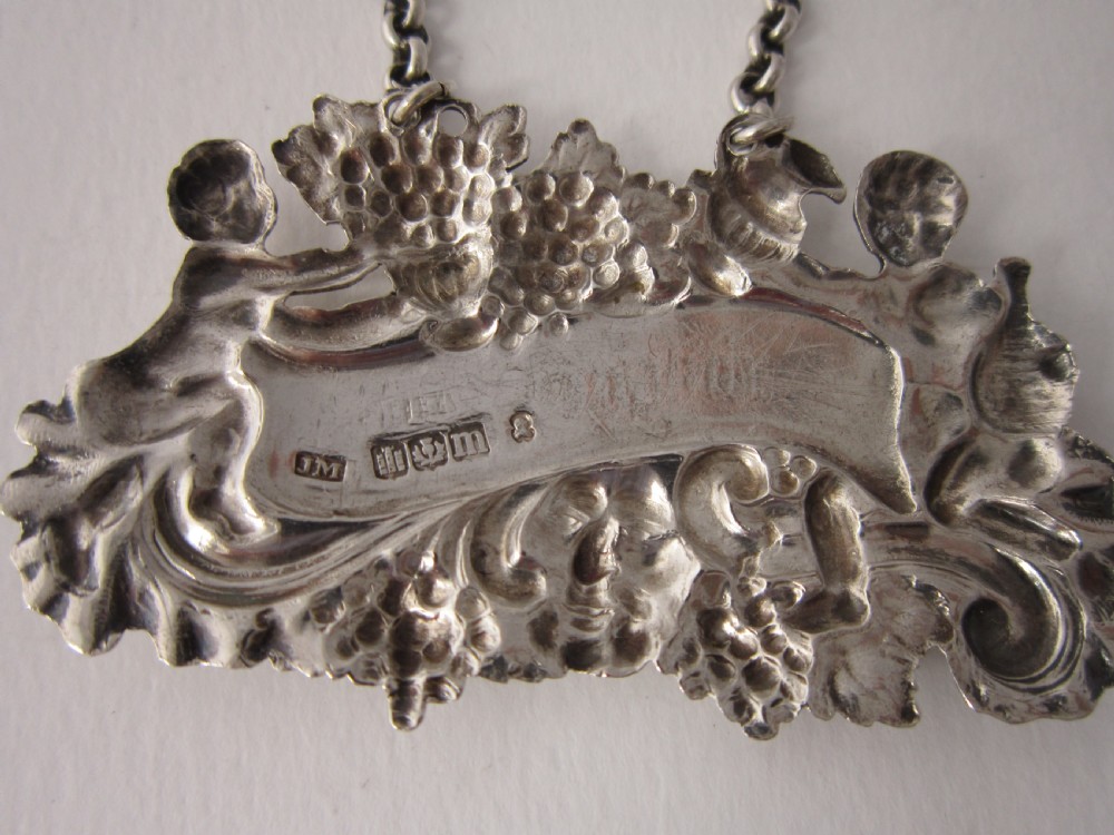 A pair of Scottish George III sterling silver decanter labels engraved with Madeira and Port, featuring relief motifs of cherubs, grapes, and scrollwork on hanging chains. View VII