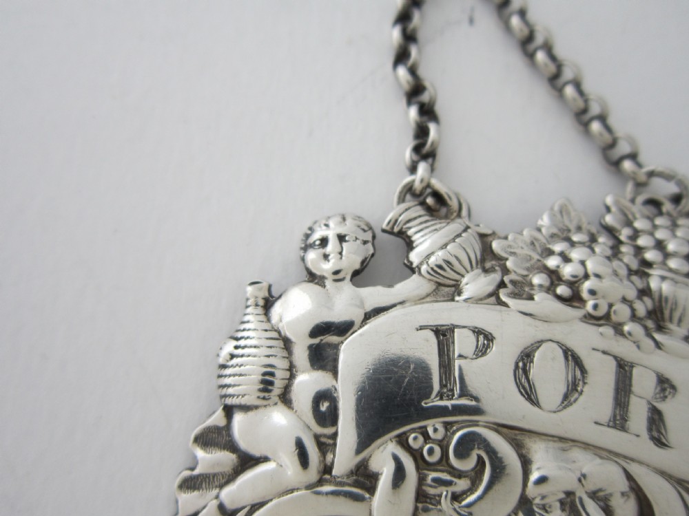A pair of Scottish George III sterling silver decanter labels engraved with Madeira and Port, featuring relief motifs of cherubs, grapes, and scrollwork on hanging chains. View IX