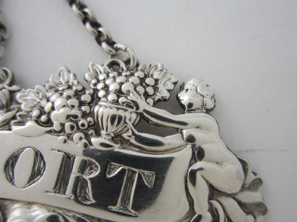 A pair of Scottish George III sterling silver decanter labels engraved with Madeira and Port, featuring relief motifs of cherubs, grapes, and scrollwork on hanging chains. View X