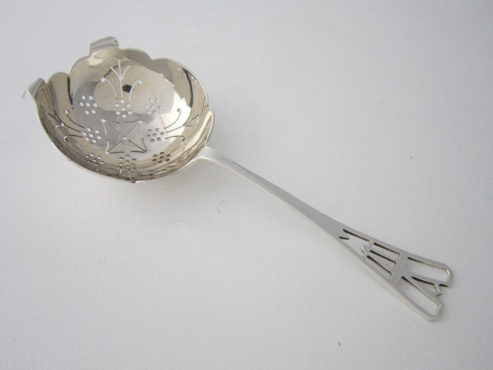 A sterling silver tea strainer featuring a pierced bowl with geometric patterns and an openwork handle.