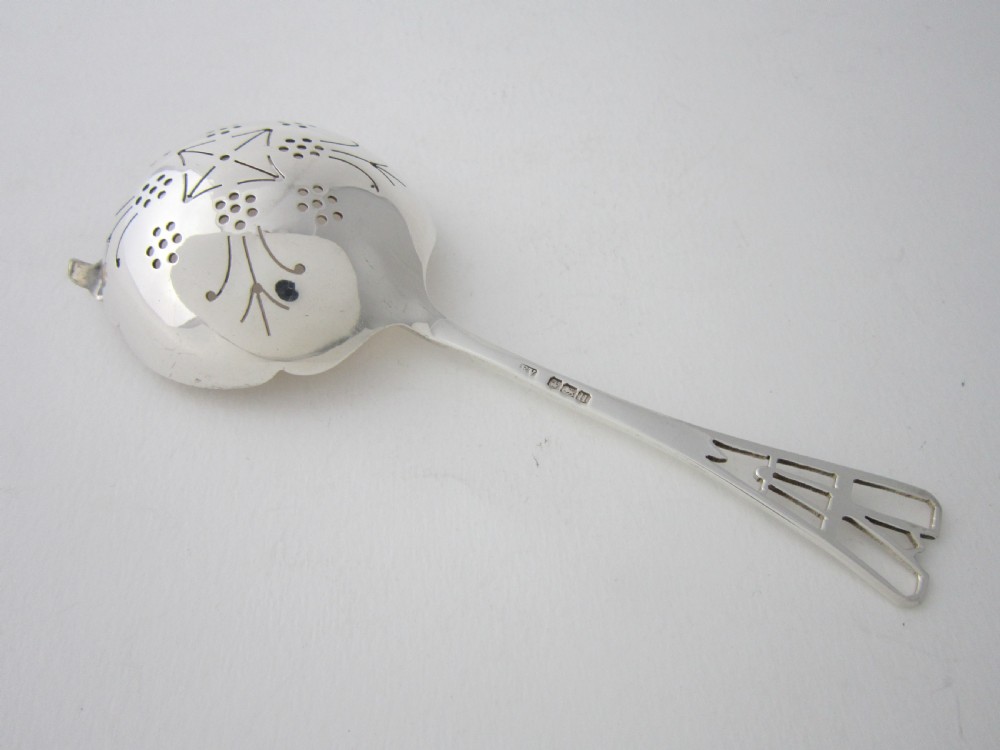 A sterling silver tea strainer featuring a pierced bowl with geometric patterns and an openwork handle. View V