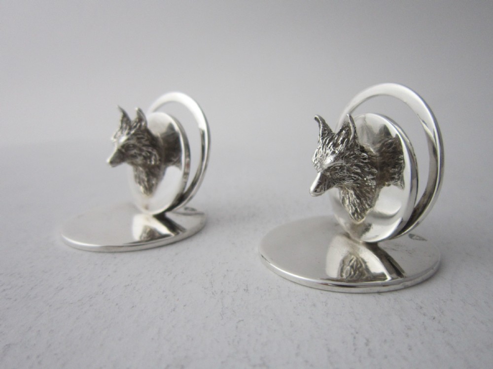 A pair of sterling silver place card holders featuring sculpted fox heads mounted on circular silver bases.