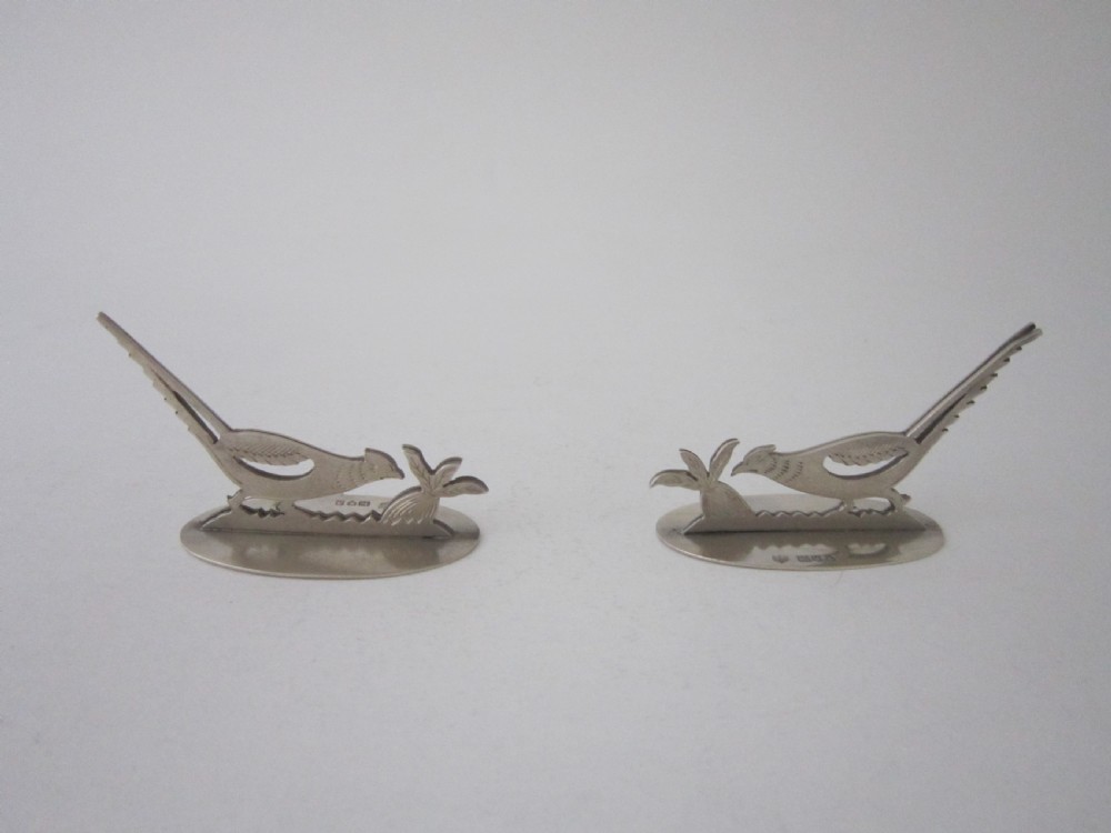 A pair of hallmarked sterling silver menu card holders featuring silhouetted pheasants set on oval bases.