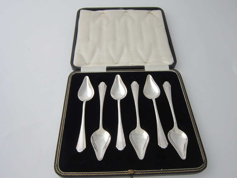 A set of six sterling silver grapefruit spoons with pointed bowls and stepped handles presented inside a fitted black velvet case.