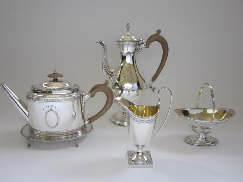 A five-piece sterling silver tea and coffee set featuring carved wooden handles, engraved oval cartouches, a teapot with stand, coffee pot, cream jug, and sugar basket.