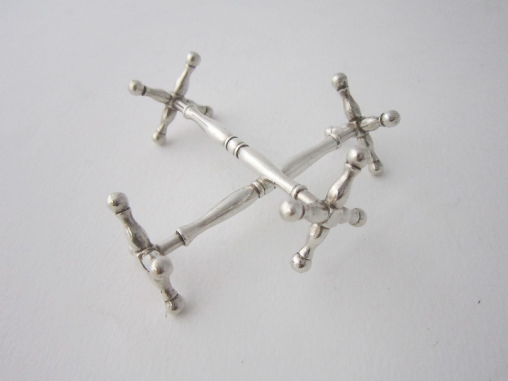 A pair of antique sterling silver knife rests featuring turned central bars and cross-shaped end supports with ball feet. View II