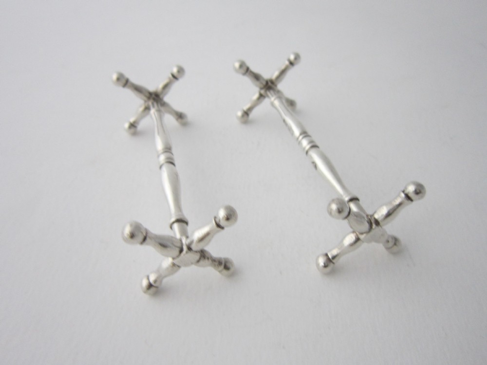 A pair of antique sterling silver knife rests featuring turned central bars and cross-shaped end supports with ball feet. View III