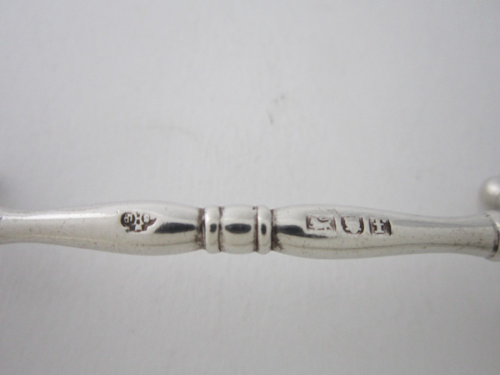 A pair of antique sterling silver knife rests featuring turned central bars and cross-shaped end supports with ball feet. View V