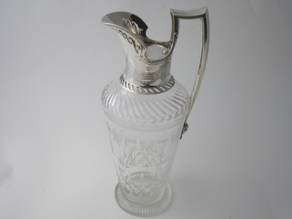 An antique Victorian claret jug featuring a clear etched glass body with cut geometric patterns and an engraved sterling silver collar and handle. View II