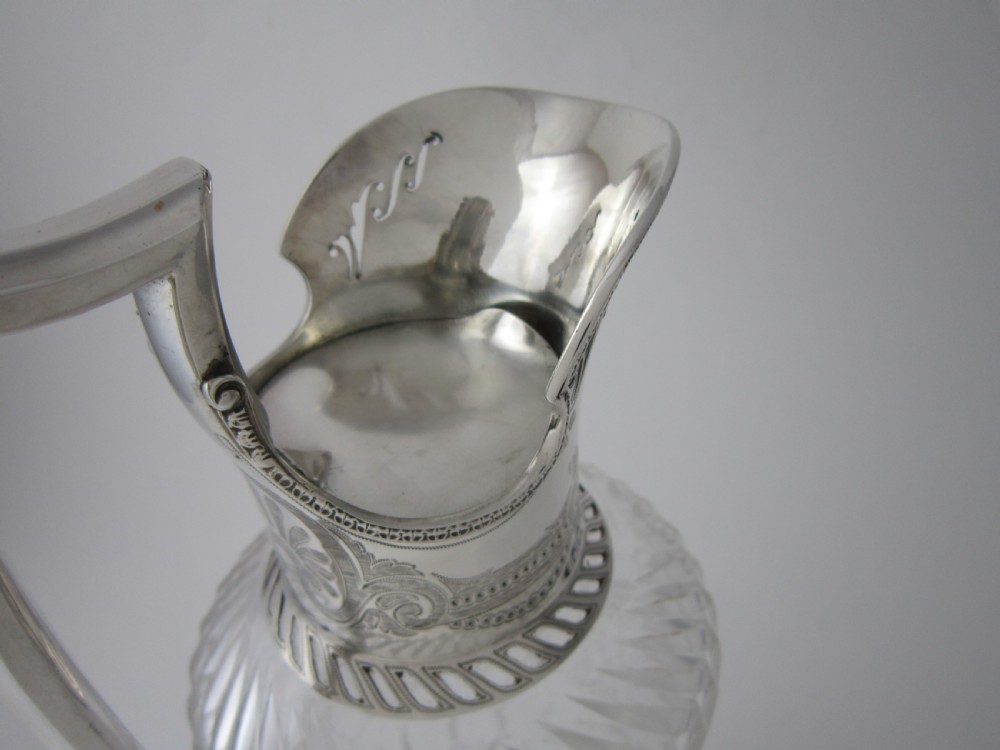 An antique Victorian claret jug featuring a clear etched glass body with cut geometric patterns and an engraved sterling silver collar and handle. View IV
