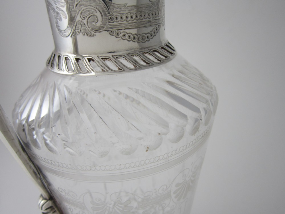 An antique Victorian claret jug featuring a clear etched glass body with cut geometric patterns and an engraved sterling silver collar and handle. View V