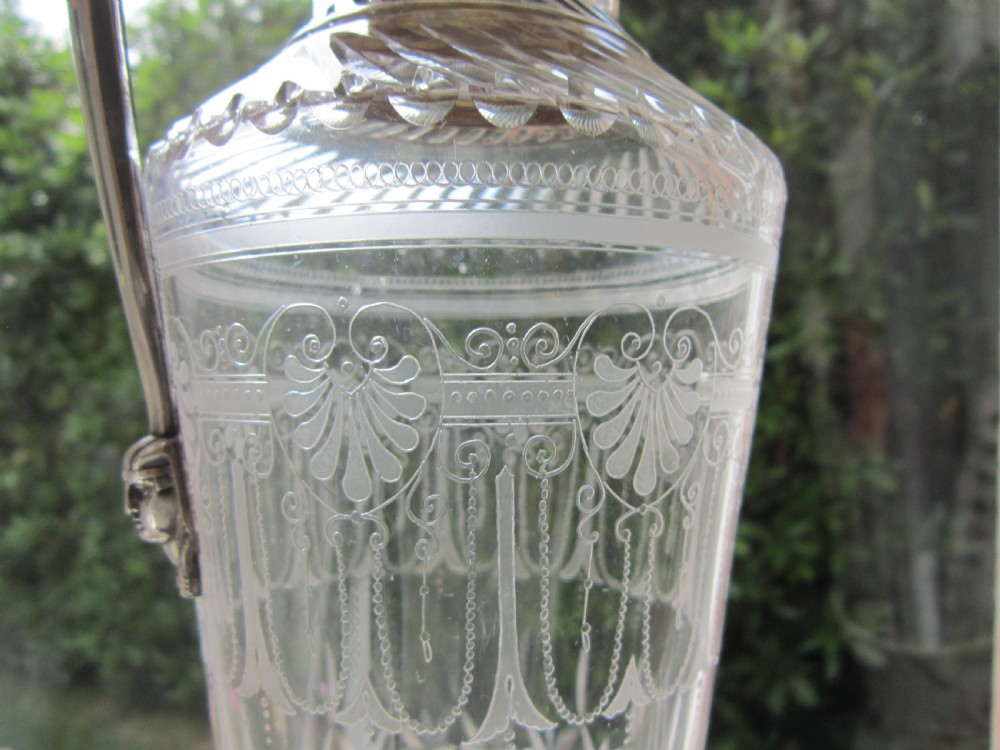 An antique Victorian claret jug featuring a clear etched glass body with cut geometric patterns and an engraved sterling silver collar and handle. View VI