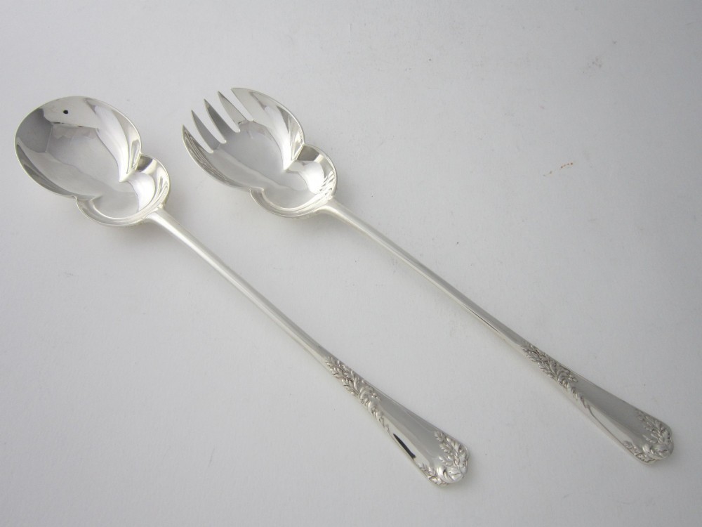 A pair of Edwardian sterling silver salad servers with chased foliate handles and shaped lobed bowls, dating to 1903.