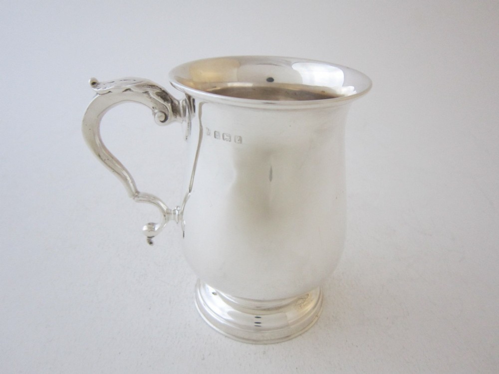 A plain sterling silver christening mug featuring a flared rim, baluster body, pedestal base, and a leaf-capped scroll handle. View III