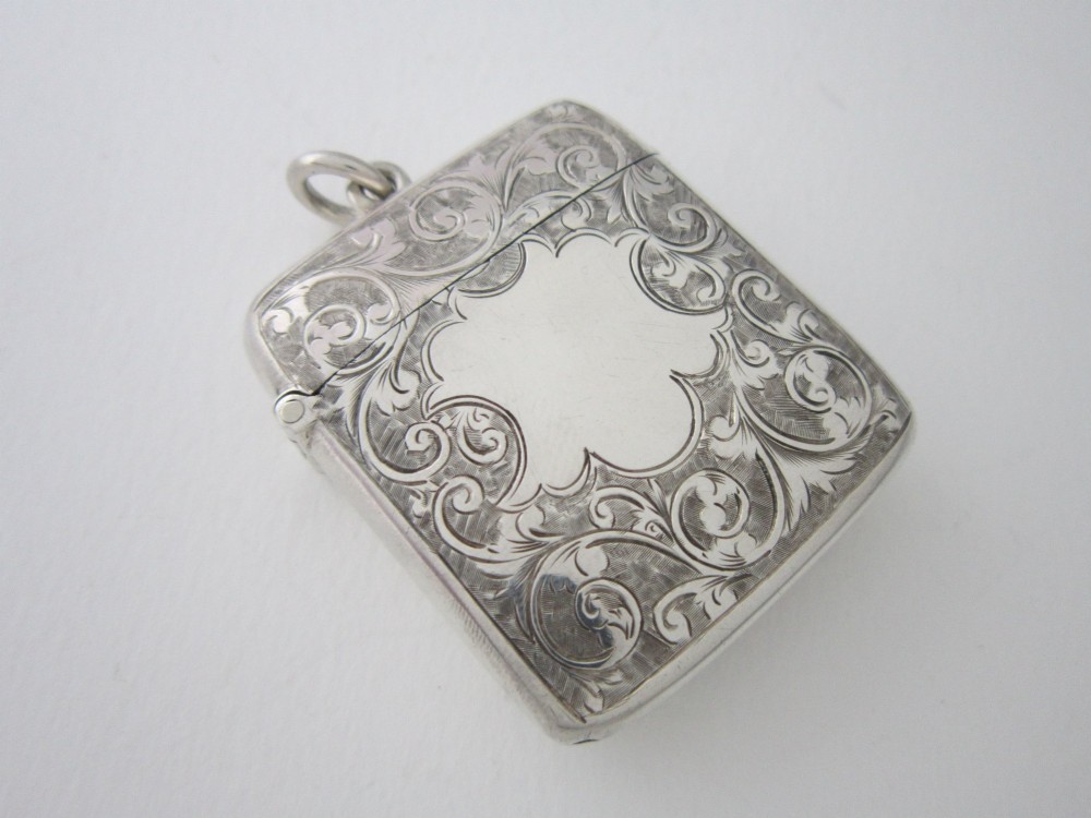 An antique sterling silver vesta case featuring hand-engraved foliate scrollwork, a vacant shield cartouche, and an attached suspension ring. View II