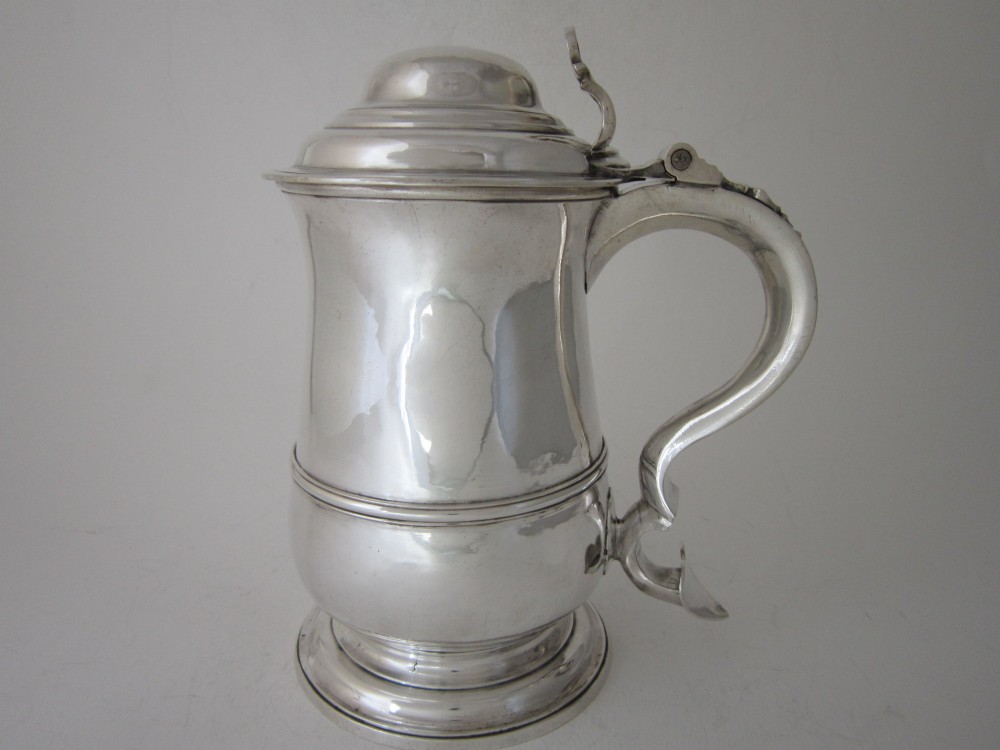 An antique George III sterling silver lidded tankard featuring a moulded dome lid, scroll handle, central girdle band, and spreading base.