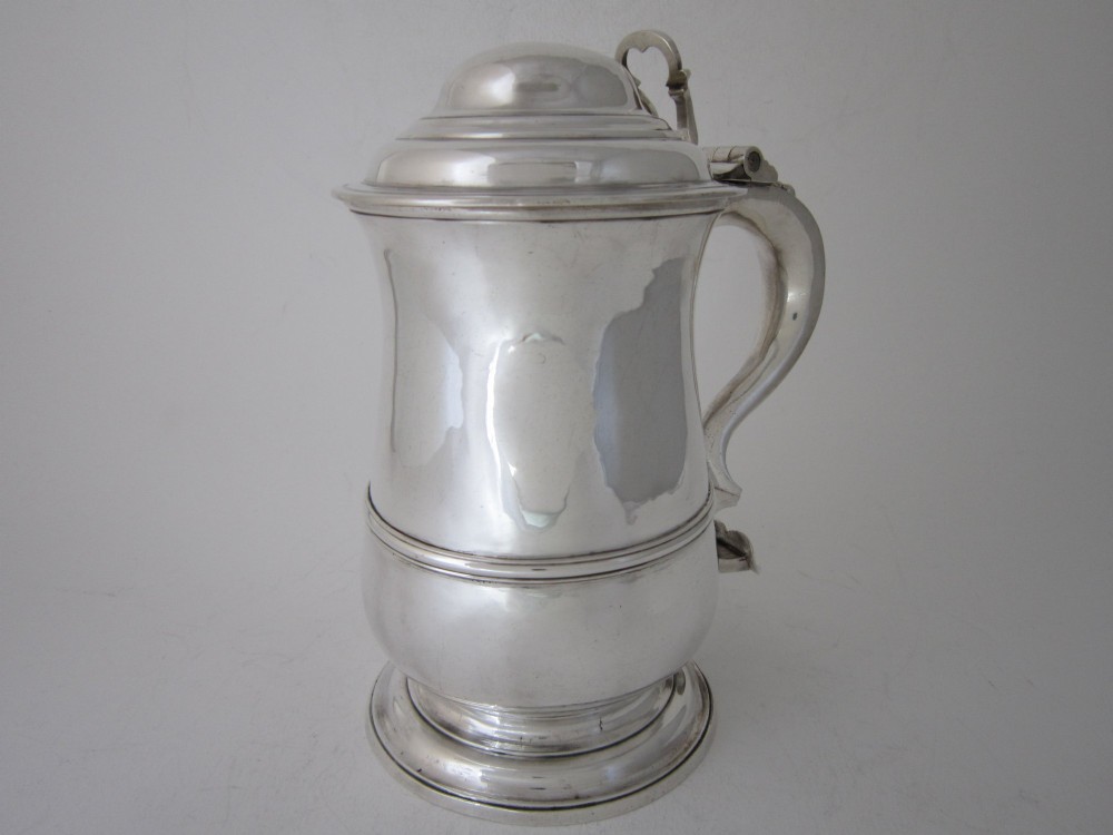 An antique George III sterling silver lidded tankard featuring a moulded dome lid, scroll handle, central girdle band, and spreading base. View II