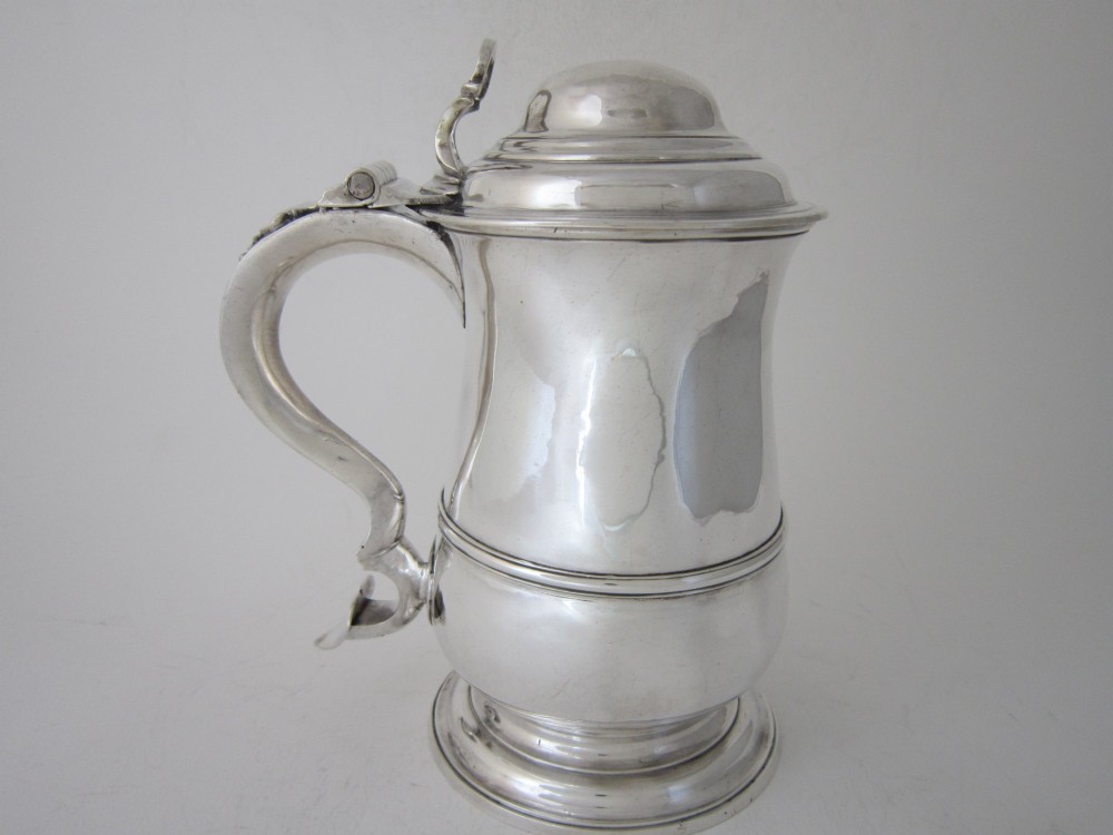An antique George III sterling silver lidded tankard featuring a moulded dome lid, scroll handle, central girdle band, and spreading base. View IV