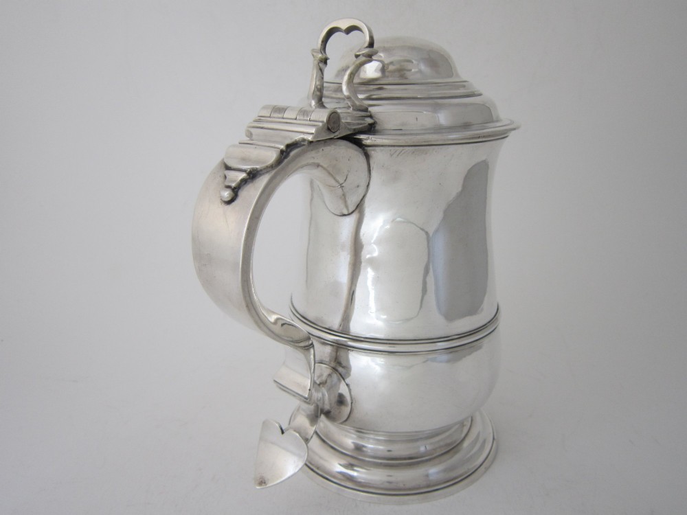 An antique George III sterling silver lidded tankard featuring a moulded dome lid, scroll handle, central girdle band, and spreading base. View V