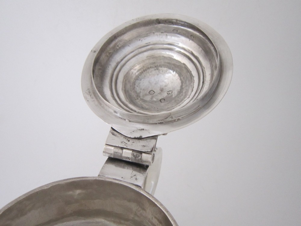 An antique George III sterling silver lidded tankard featuring a moulded dome lid, scroll handle, central girdle band, and spreading base. View VI