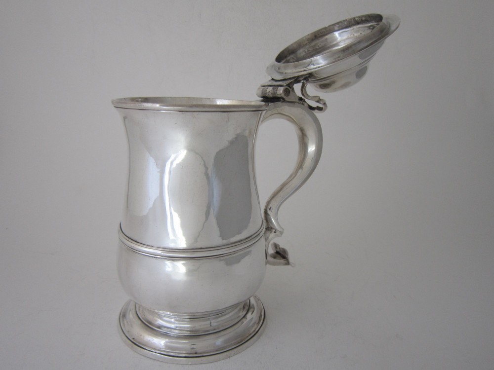 An antique George III sterling silver lidded tankard featuring a moulded dome lid, scroll handle, central girdle band, and spreading base. View X