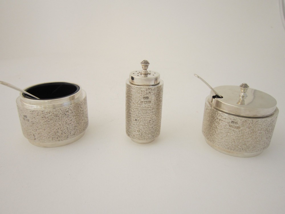 A three-piece sterling silver condiment set with textured bark-effect surfaces including a salt cellar, mustard pot, pepper shaker, and two spoons in a blue fitted case. View III