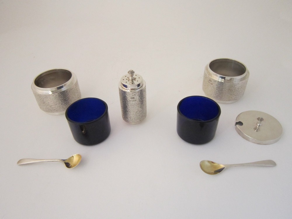 A three-piece sterling silver condiment set with textured bark-effect surfaces including a salt cellar, mustard pot, pepper shaker, and two spoons in a blue fitted case. View IV