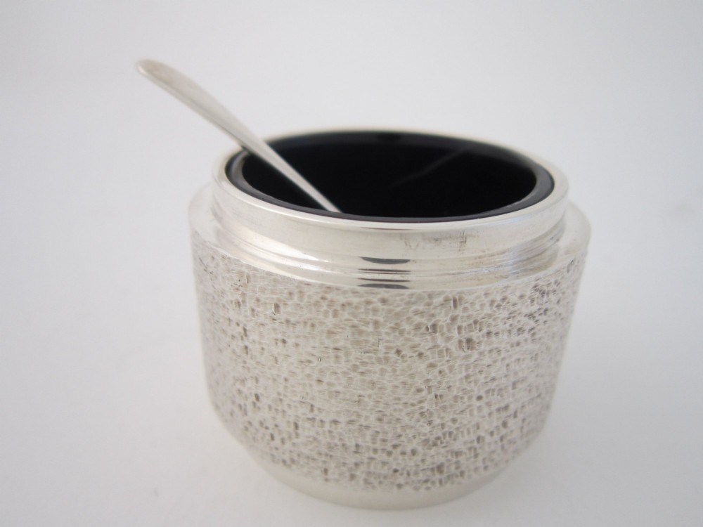 A three-piece sterling silver condiment set with textured bark-effect surfaces including a salt cellar, mustard pot, pepper shaker, and two spoons in a blue fitted case. View VII
