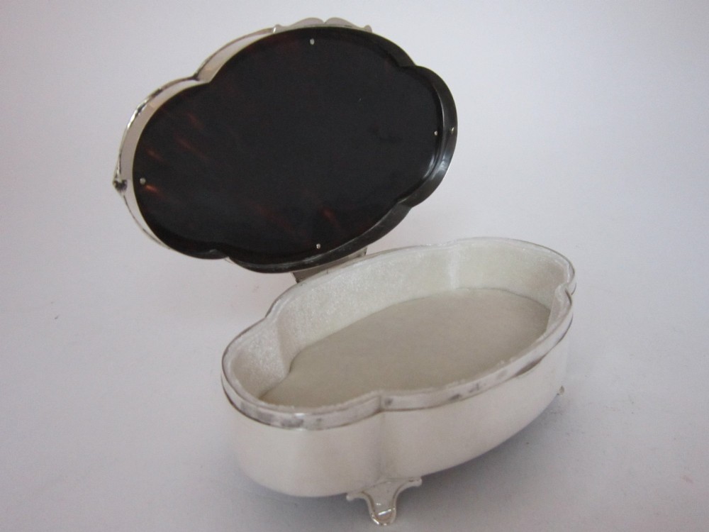 A shaped sterling silver trinket box featuring a dark tortoiseshell lid inlaid with a silver flower basket and ribbon swags, resting on four small feet. View IV