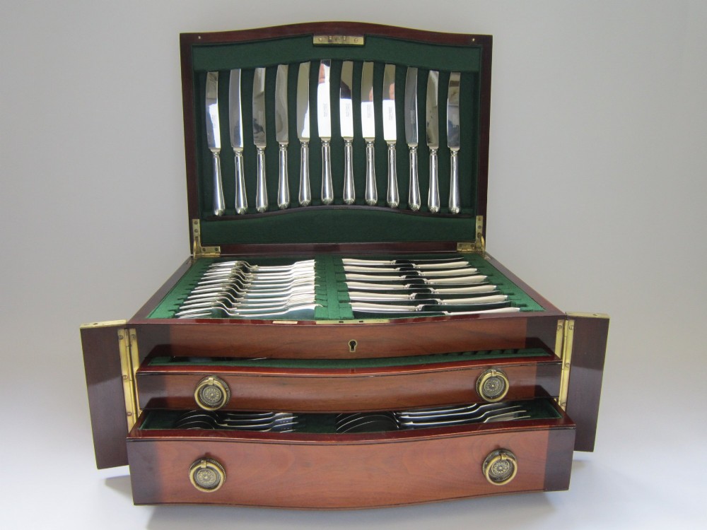An open Victorian mahogany canteen chest fitted with drawers displaying a full sterling silver fiddle pattern cutlery service lined in green fabric.